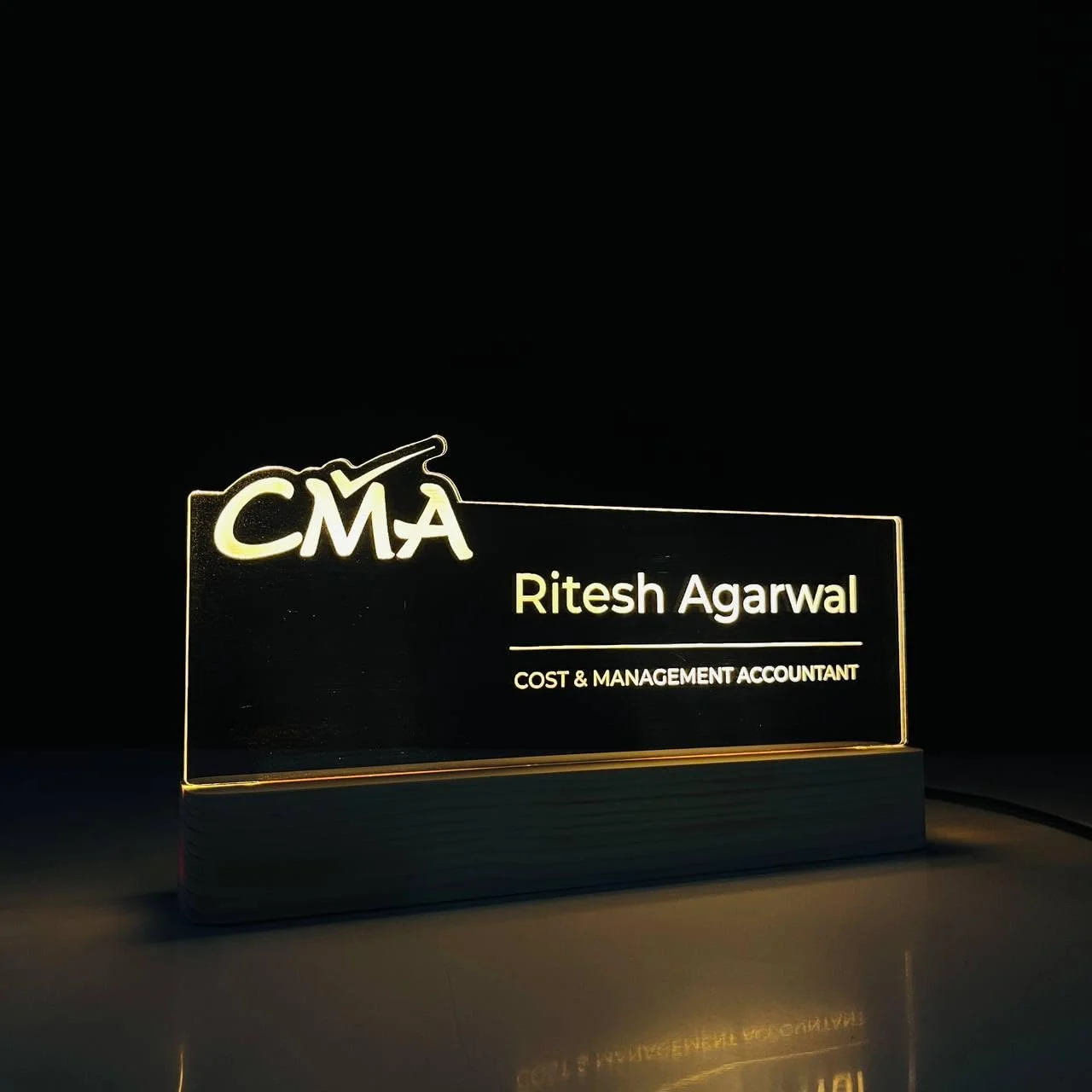 Personalised Name Lamp with Wooden Base for Cost & Management Accountants – 10 x 6 inch – glowing on a desk